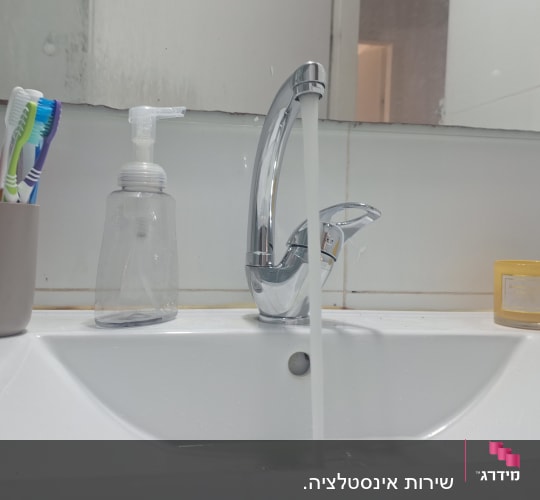 ברז מים זורם בכיור עם מברשות שיניים וסבון